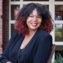 Photo of Brandi Collins-Dexter, a Black woman with curly hair, sitting outside wearing a black shirt