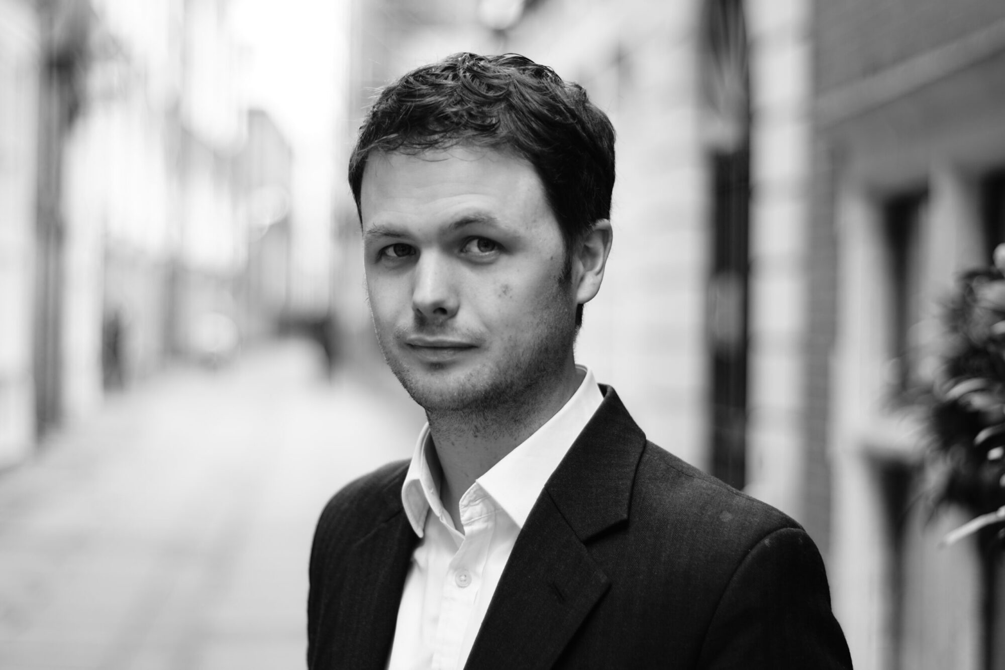 A man, Michael Hallsworth, stands looking at the camera with a pedestrian street behind him