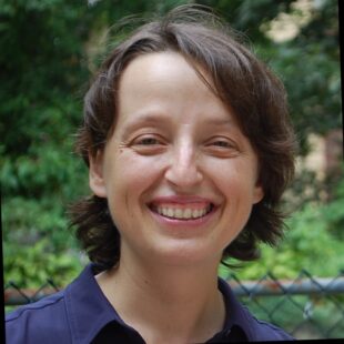 photo of Emine Dogan, a light-skinned woman with short brown hair, wearing a blue shirt, smiling, outside