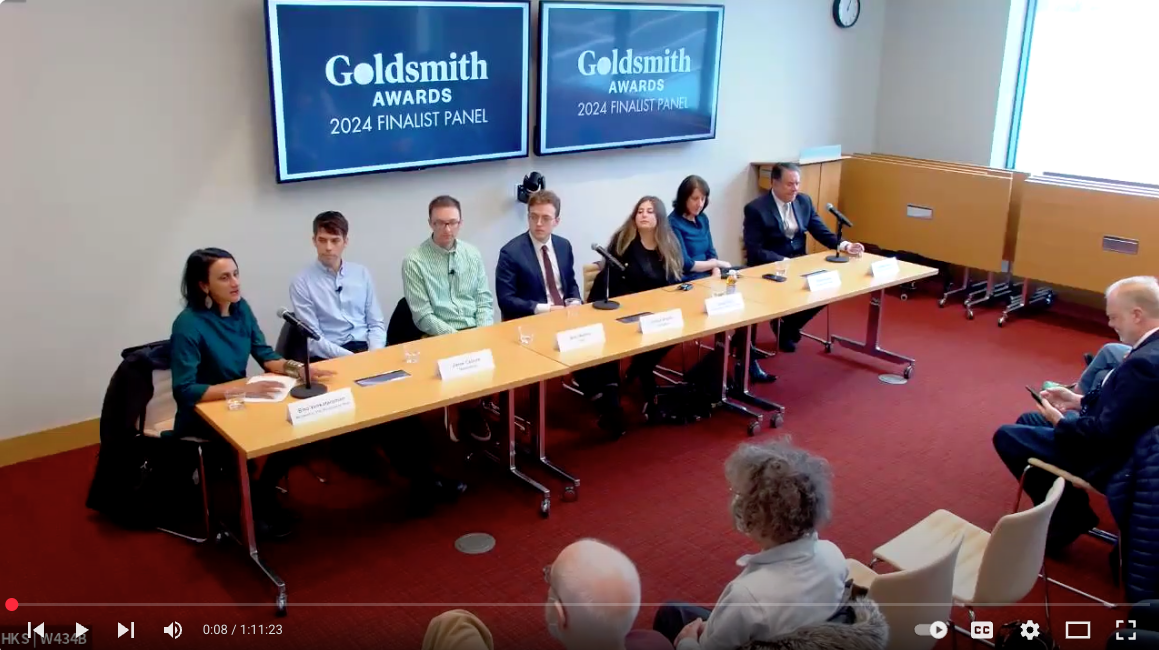 Bina Venkataraman moderates a panel of six journalists, all finalists for the Goldsmith Prize for Investigative Reporting. They sit behind a long table in a room, with the front row of the audience visible.