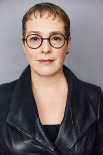 Julia Angwin, a light skinned woman with short brown hair and glasses wearing a dark blue leather jacket
