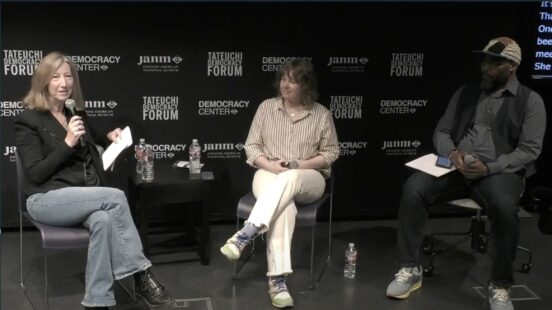 Three individuals sitting on a stage with a microphone in hand