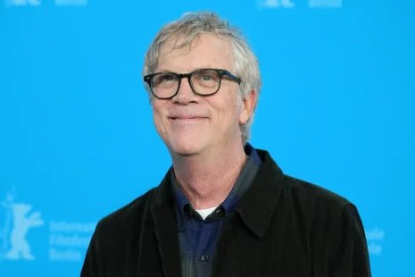 Man with glasses smiling in front of a blue background