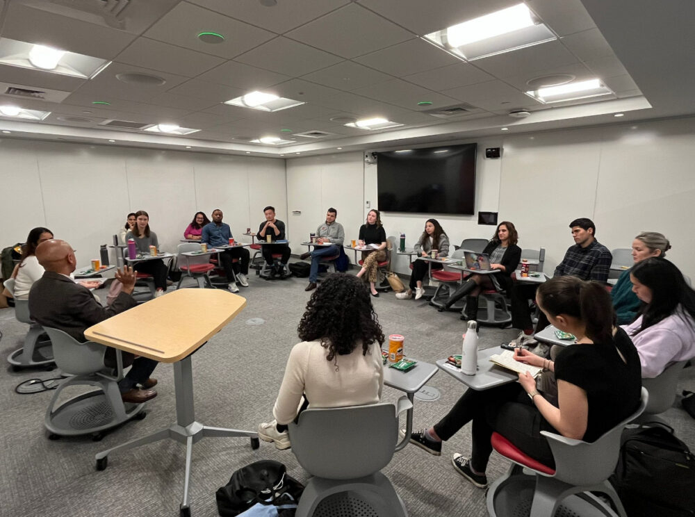 A photo of a BISG student workshop shows a group of students in a classroom, sitting in chairs arranged in a large circle.