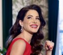 Julia Allison, a light skinned woman with long dark hair, wearing a red dress, looks over her shoulder at the camera