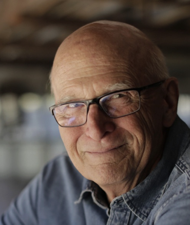 Jon Else, a light skinned bald man wearing glasses and a blue collared shirt