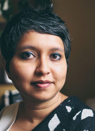 Pooja Rangan, a medium-skinned woman with short dark hair wearing a black and white print shirt and blue eyeliner