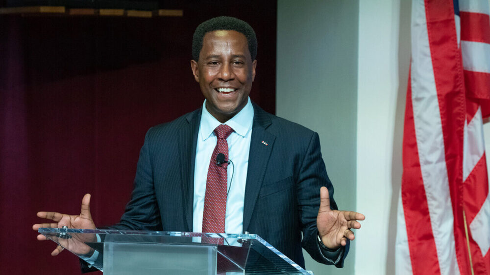 Setti Warren stands at a lecturn, smiling and gesturing widely