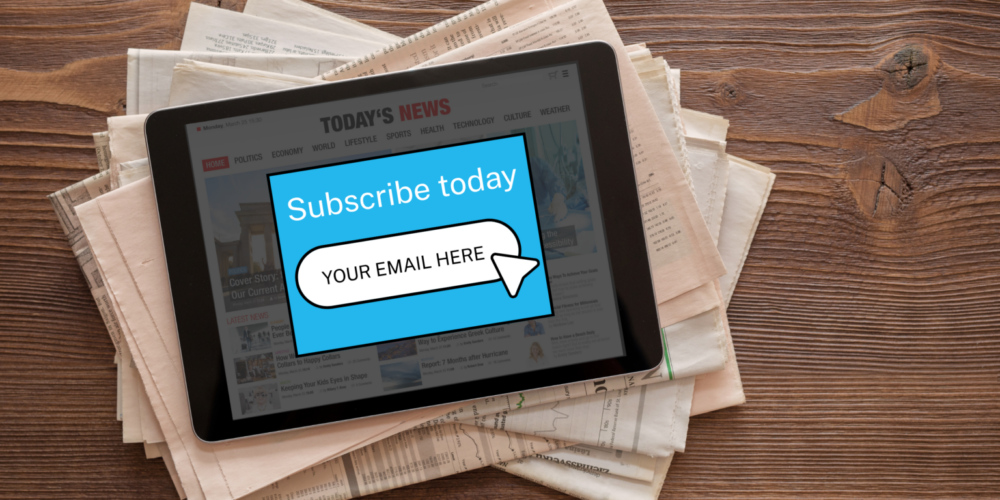 Tablet displaying a news website with a pop-up that says “Subscribe today” and an email sign-up field, resting on a stack of newspapers on a wooden table.