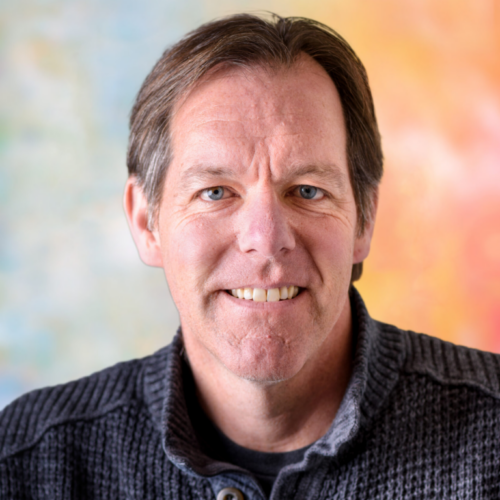Mike Beaudet, a light skinned person with short brown hair looks into the camera wearing a dark blue plaid shirt