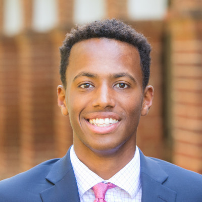 Headshot of a smiling man in a blue suit in front of a blurred background