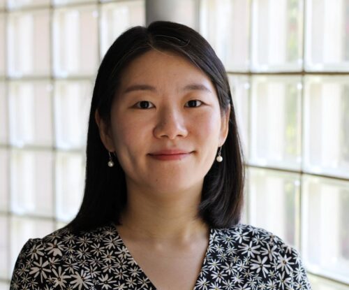 Headshot of a smiling woman in front of a glass wall