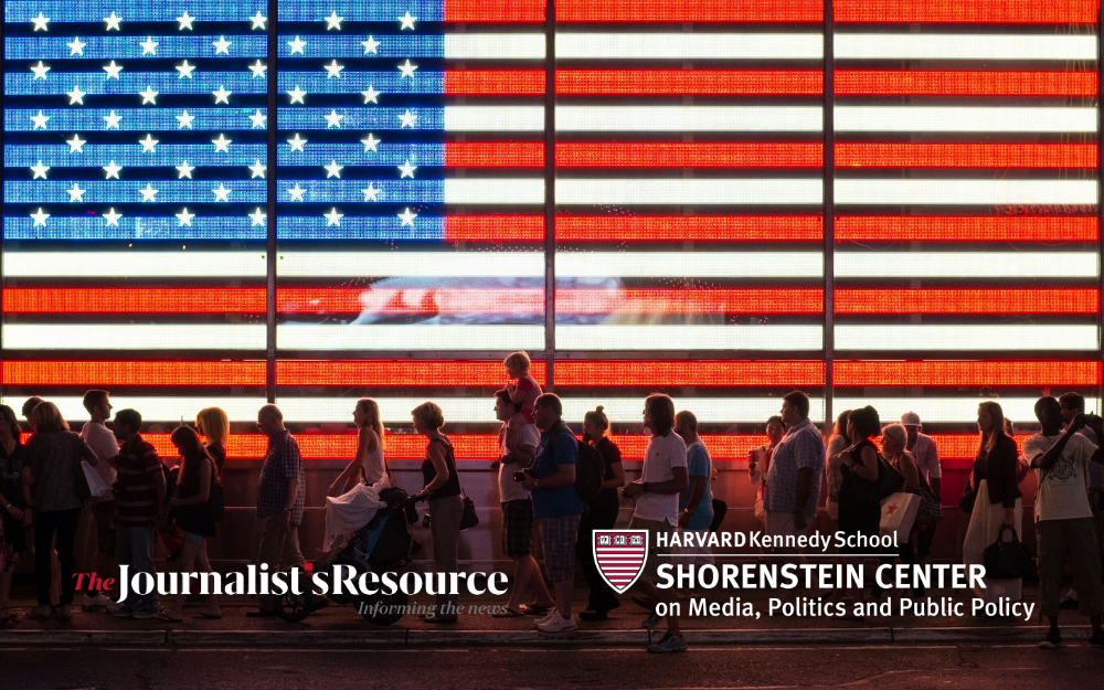 People walk in front of a large illuminated American flag, with logos for The Journalist’s Resource and the Shorenstein Center.