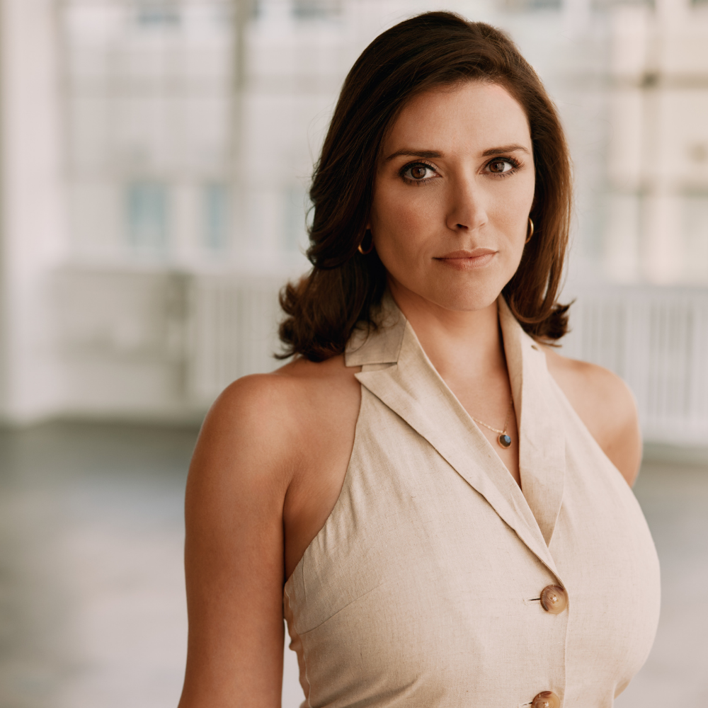 Portrait of a woman with shoulder-length brown hair wearing a sleeveless cream-colored top in a bright indoor setting.