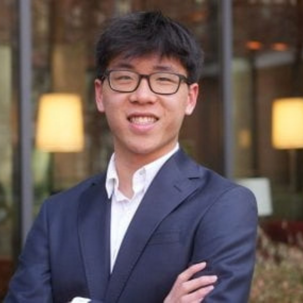 Headshot of a smiling man with dark hair and glasses, wearing a navy suit jacket and white shirt with his arms crossed.