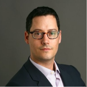 photo of Ben Monnie, a light skinned man with short dark hair wearing glasses and a button down shirt with a dark suit jacket.