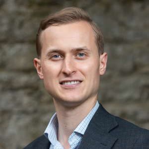 Dr. Rakoen Maertens, a light skinned man with short light brown hair wearing a shirt and jacket, stands in front of a stone wall